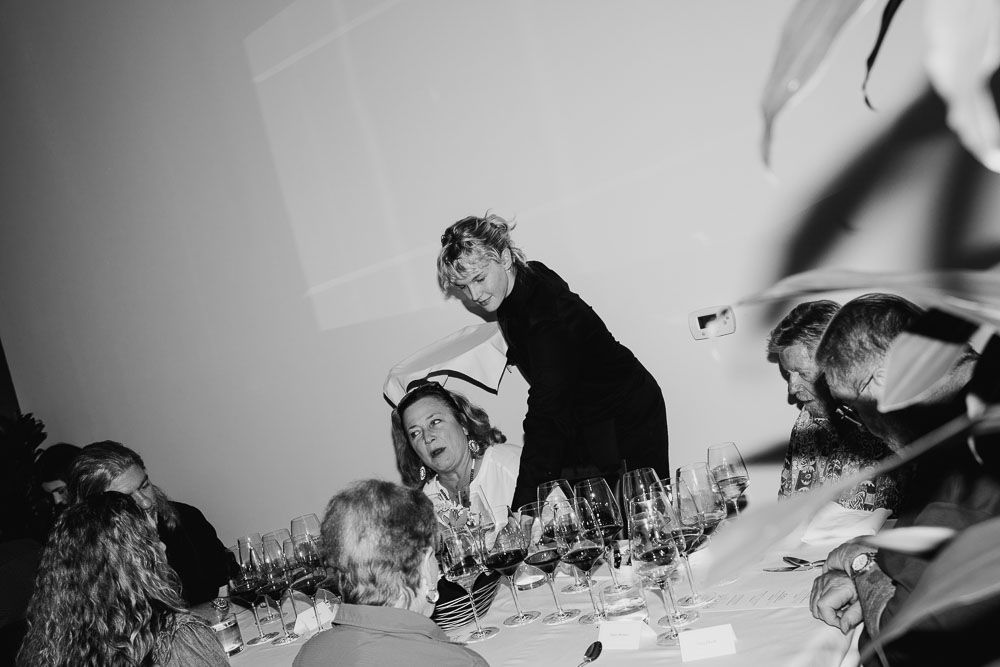 Overhead view of guests at a formal dining event with wine glasses and table settings in black and white.