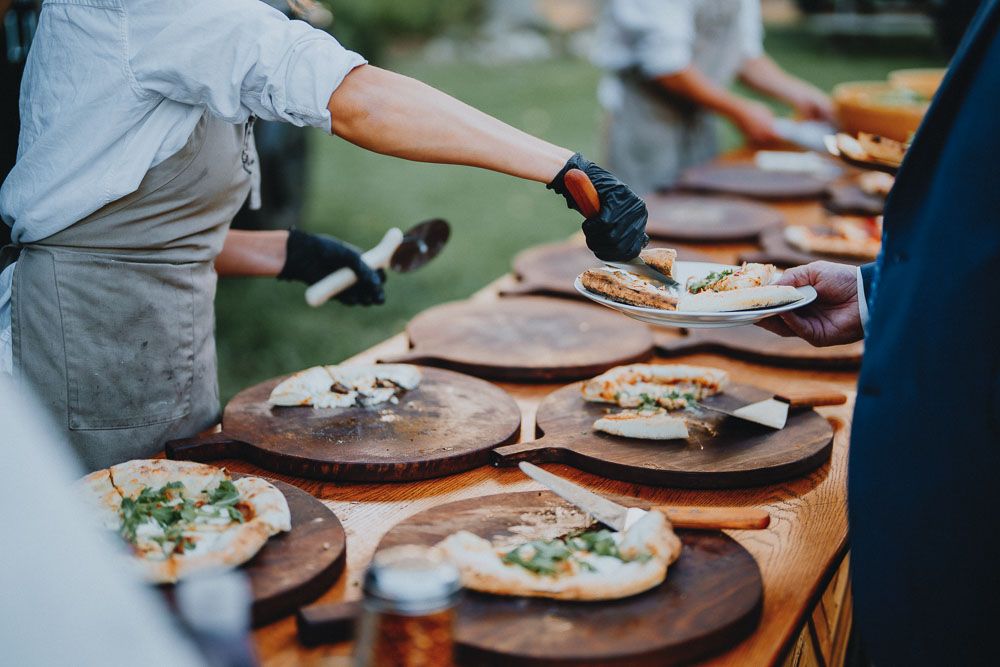 Fresh pizzas being prepared on wooden serving boards at an outdoor catering event.
