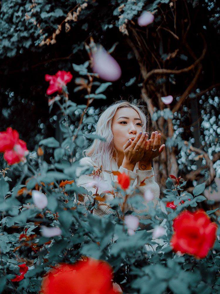 Dreamy portrait in a garden with red roses and soft lighting creating a mystical atmosphere.
