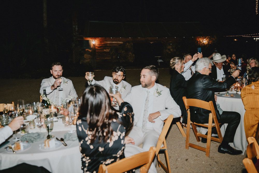 Guests enjoying an outdoor wedding reception dinner at tables decorated with glassware and place settings at night.