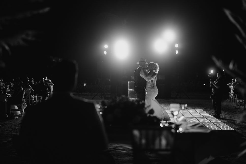 Dramatic black and white shot of newlyweds dancing on an illuminated dance floor.