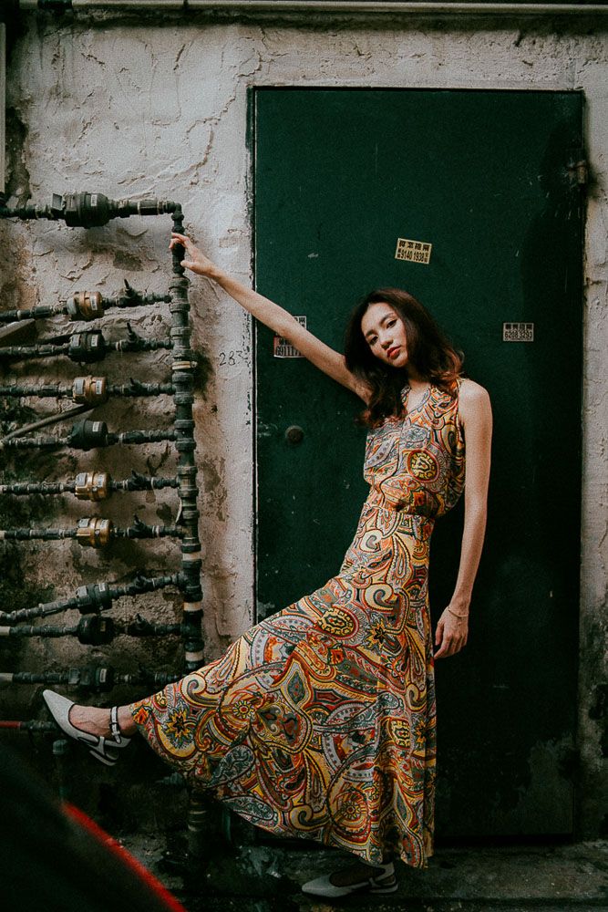 Fashion shoot with paisley print dress against industrial wall and dark doorway.