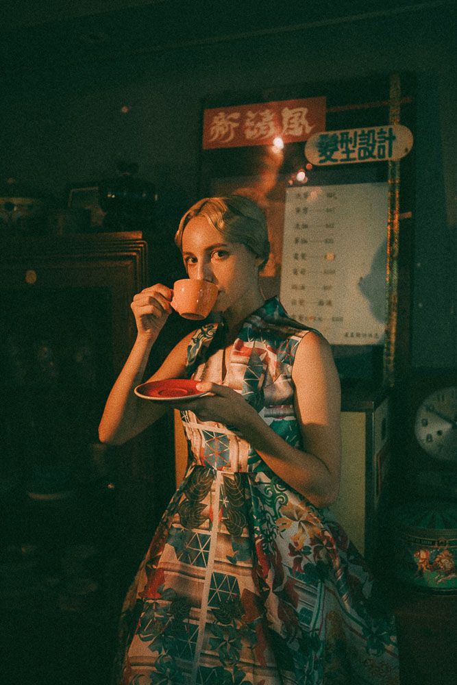 Person in patterned dress drinking tea at Asian restaurant with vintage ambiance.