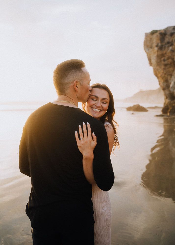 A joyful embrace captured during golden hour with dramatic coastal cliffs and ocean views.