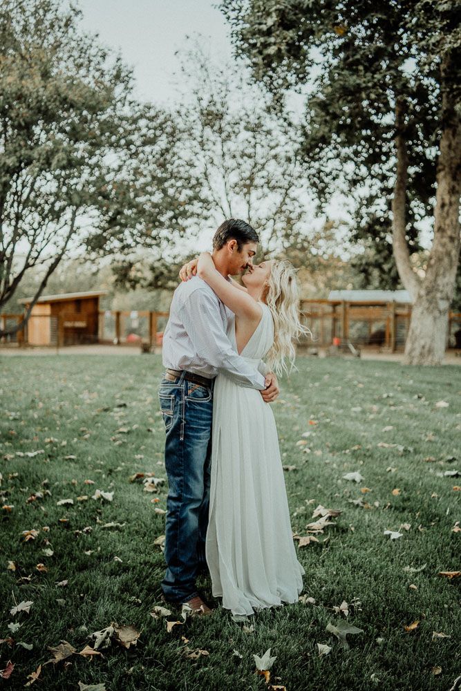 Romantic outdoor portrait on grassy lawn with trees in background.