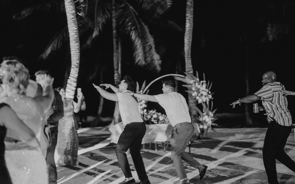 People dancing together under palm trees on a patterned dance floor at night.