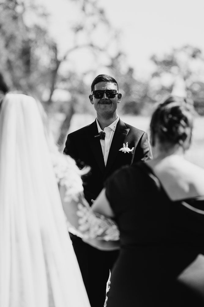 Black and white wedding ceremony photo with groom in sunglasses and tuxedo during the vows.