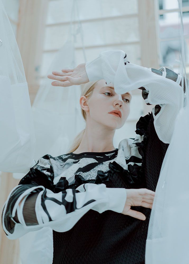 Editorial fashion shot with model in black and white graphic sweater against white architecture.