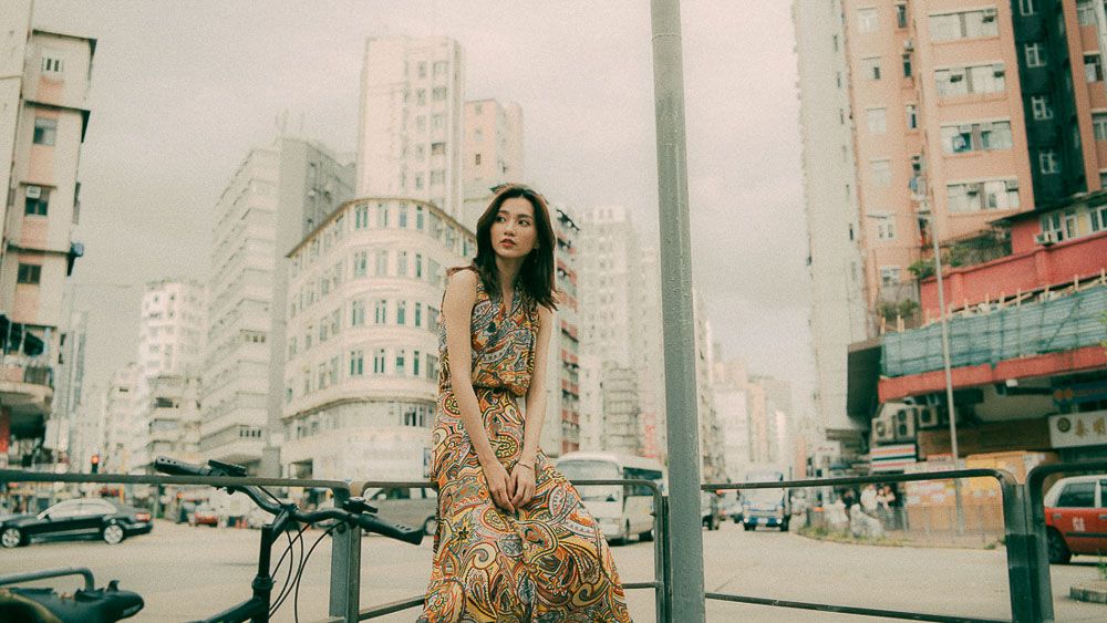 A striking urban fashion shoot featuring a paisley print dress against an industrial cityscape background.