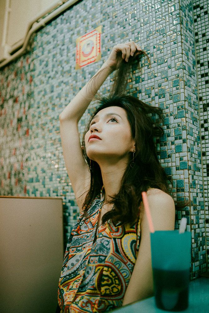 Artistic portrait against turquoise mosaic wall wearing a patterned dress with bohemian style.