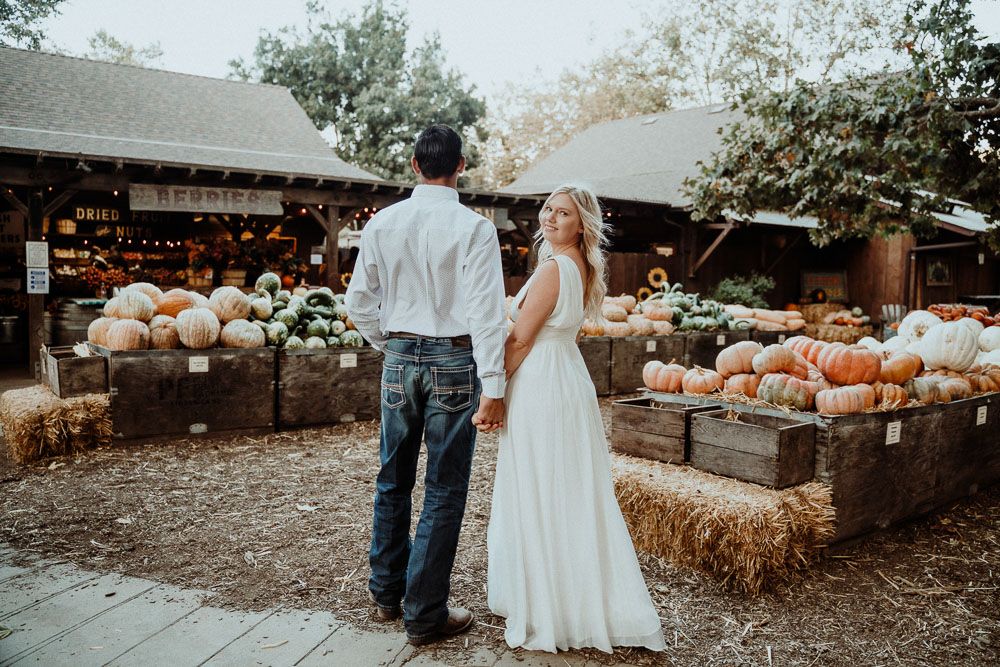 A romantic fall engagement photoshoot in a rustic pumpkin patch with hay bales and autumn decor.