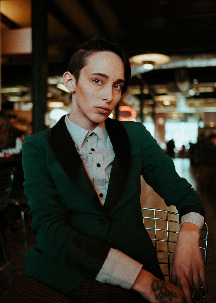 Atmospheric portrait featuring emerald green blazer and collared shirt in dim lighting.