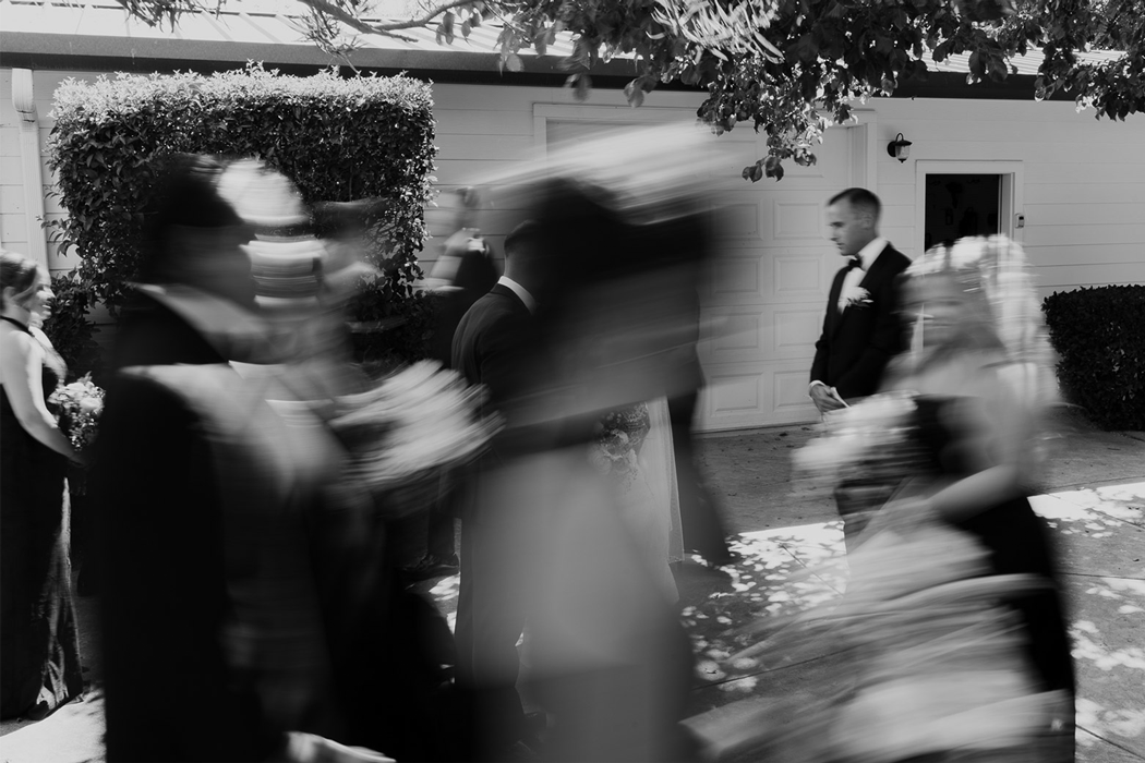 A blurred black and white motion photograph shows people walking through an urban setting.