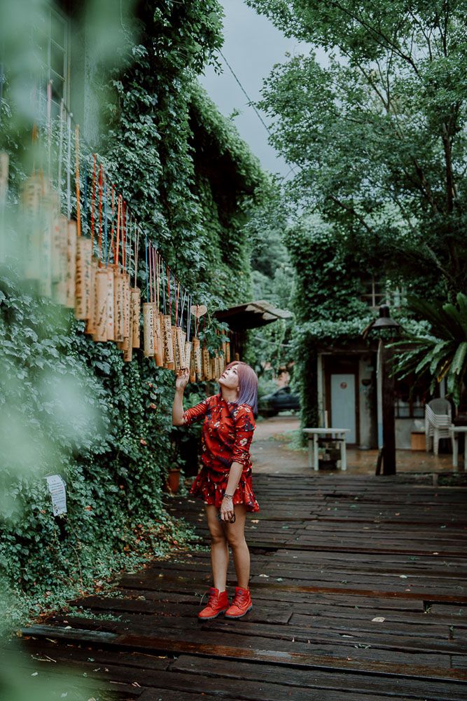 Figure in red outfit stands on wooden walkway surrounded by lush greenery.
