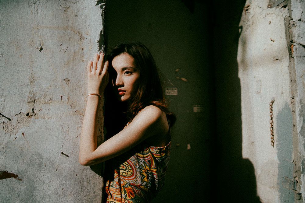 Artistic fashion photography with dramatic shadows against dark architectural backdrop.