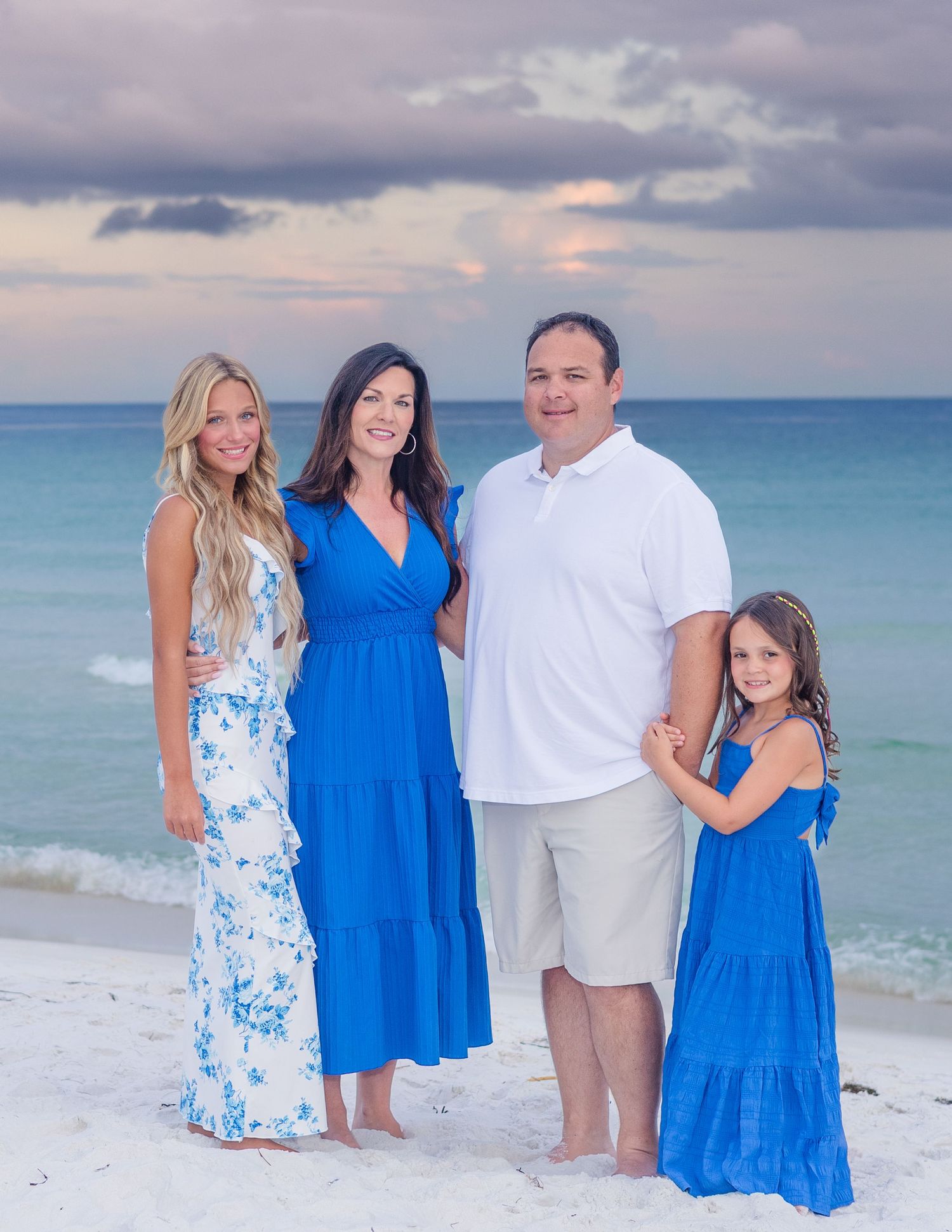 Family beach portrait with coordinating blue and white outfits against ocean backdrop.