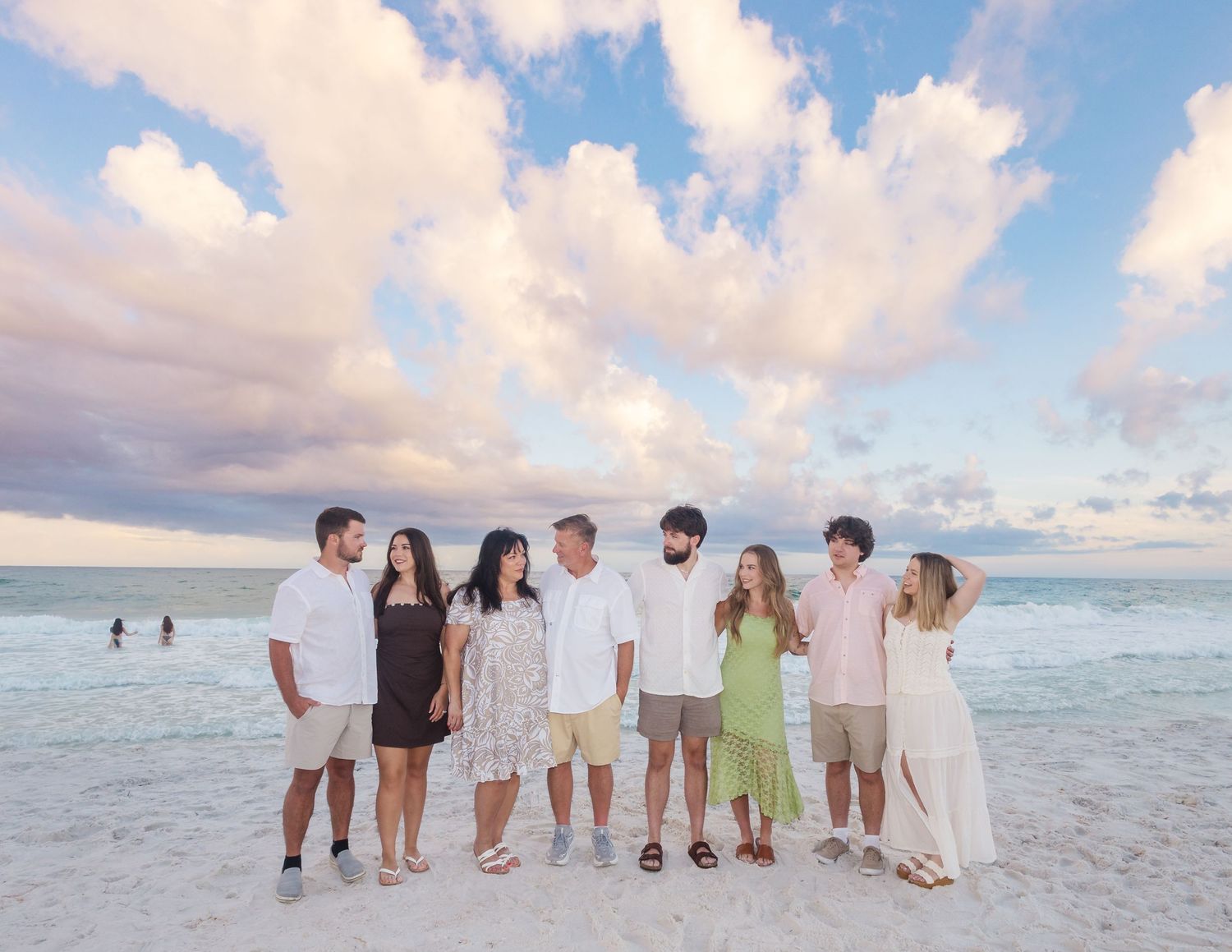 Group of friends posing together on a sandy beach at sunset with colorful clouds in the background.