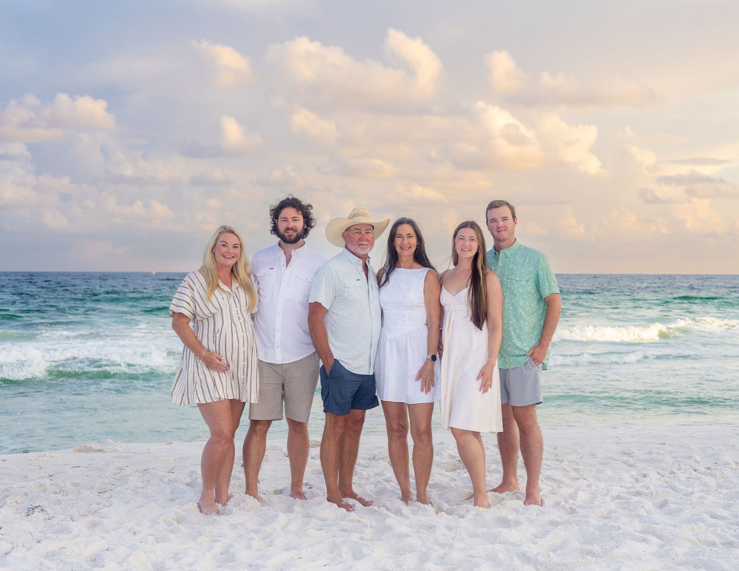 A series of beach family portraits showing people in coordinated white and pastel outfits posing on a sandy shoreline at sunset.