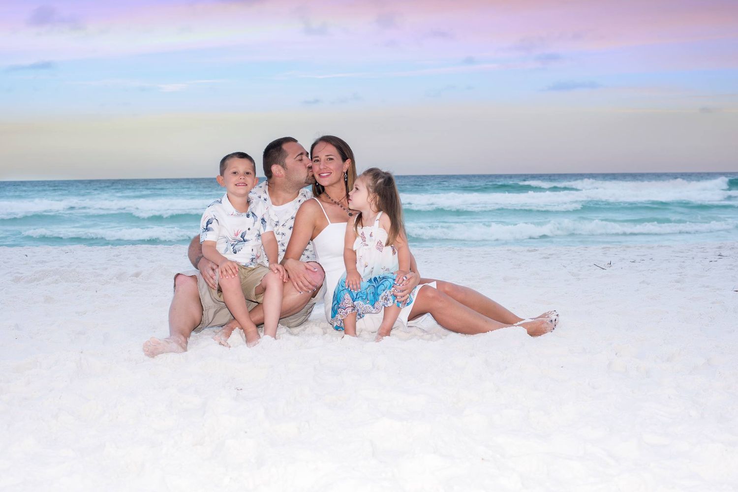 People relaxing together on a white sandy beach with turquoise ocean waves in the background.