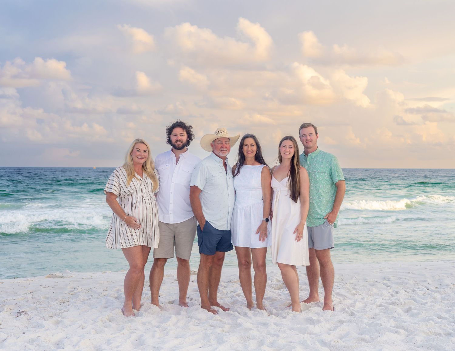 Group of people standing together on a white sandy beach with turquoise ocean waves in the background at sunset.