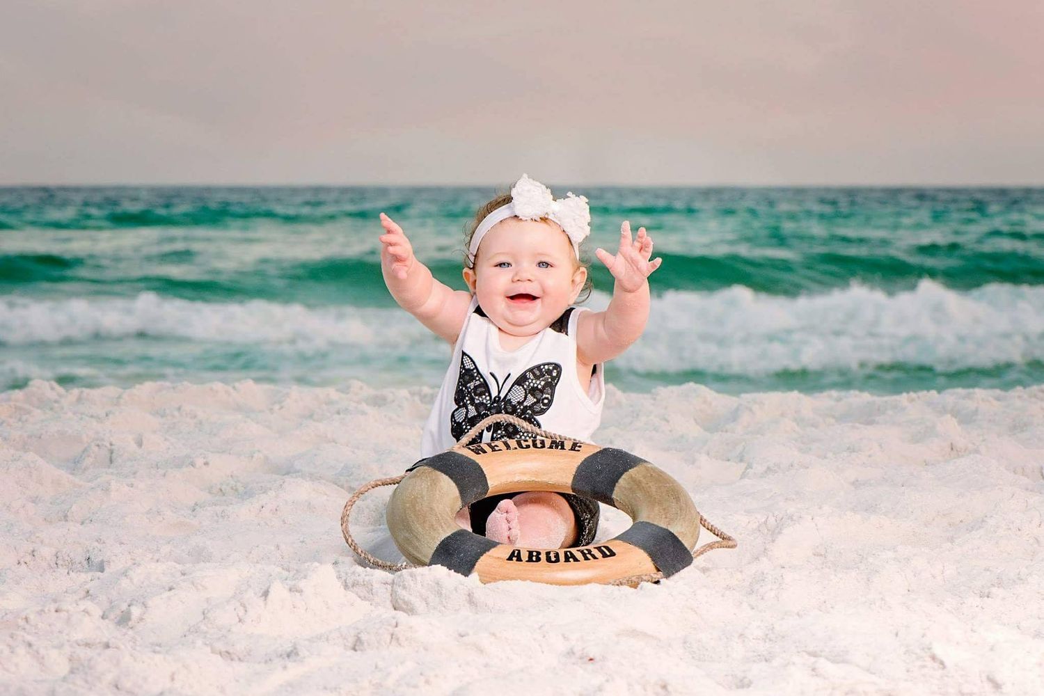 A series of six beach photos showing a joyful baby playing and sitting in the sand by turquoise ocean waves.