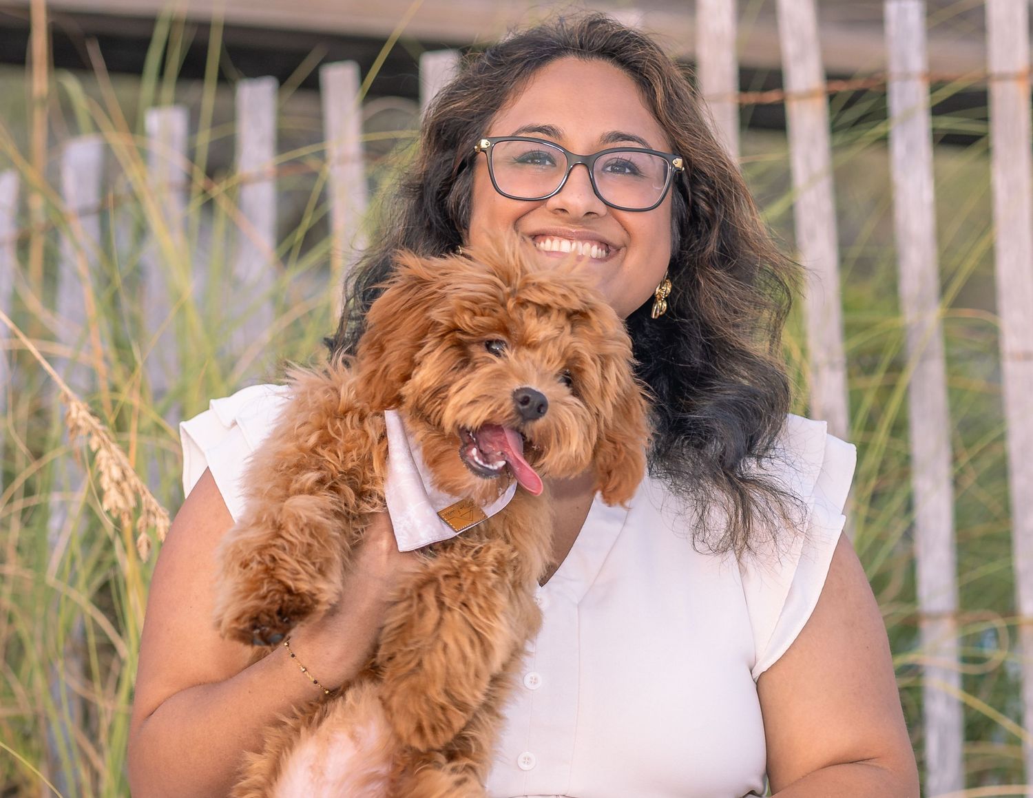 Happy golden doodle dog with glasses sitting outdoors in natural setting.