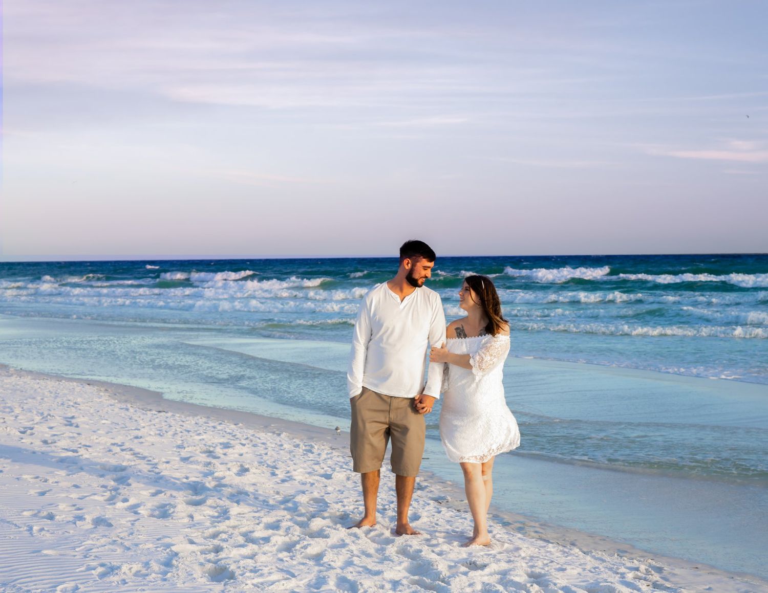 Couple walking along a pristine white sand beach with turquoise ocean waters in the background.