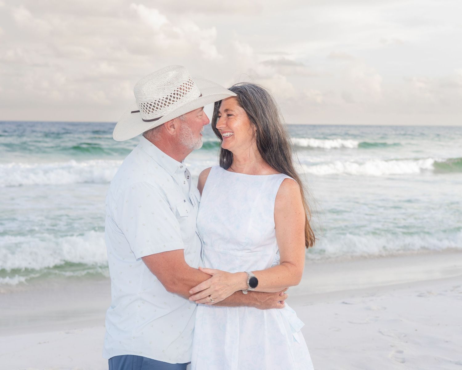 Romantic beach photoshoot of couple in white attire against ocean backdrop.