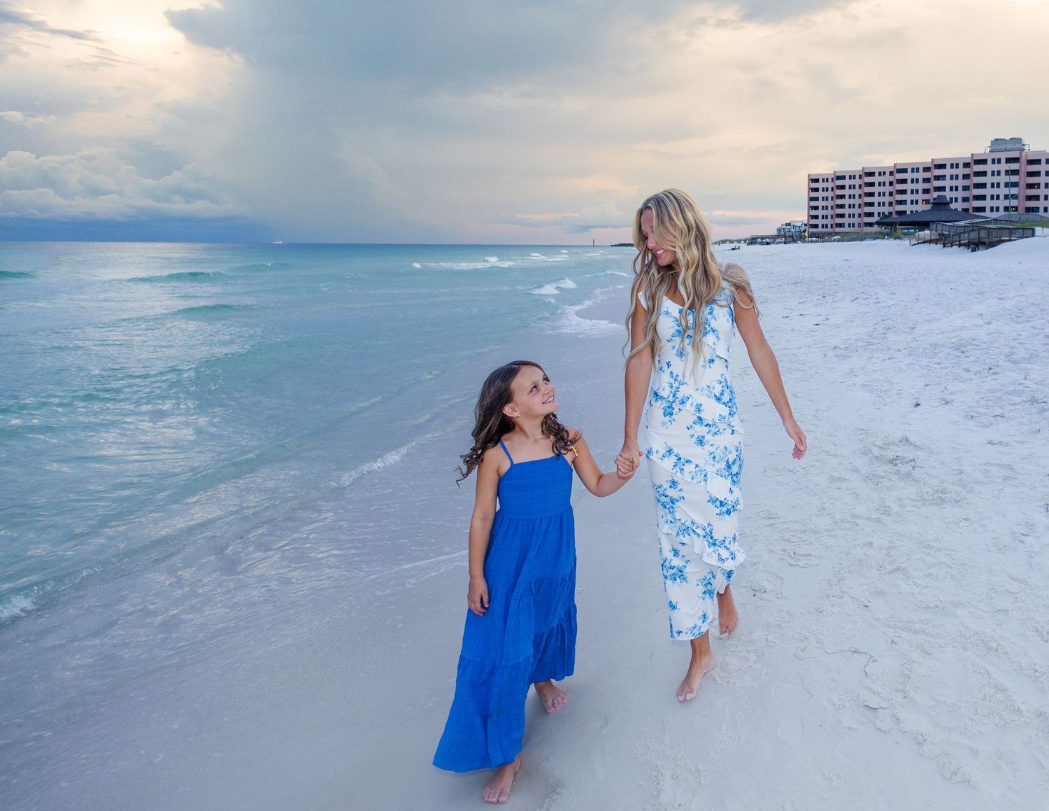 Family members walking and playing together on white sandy beach with ocean view.