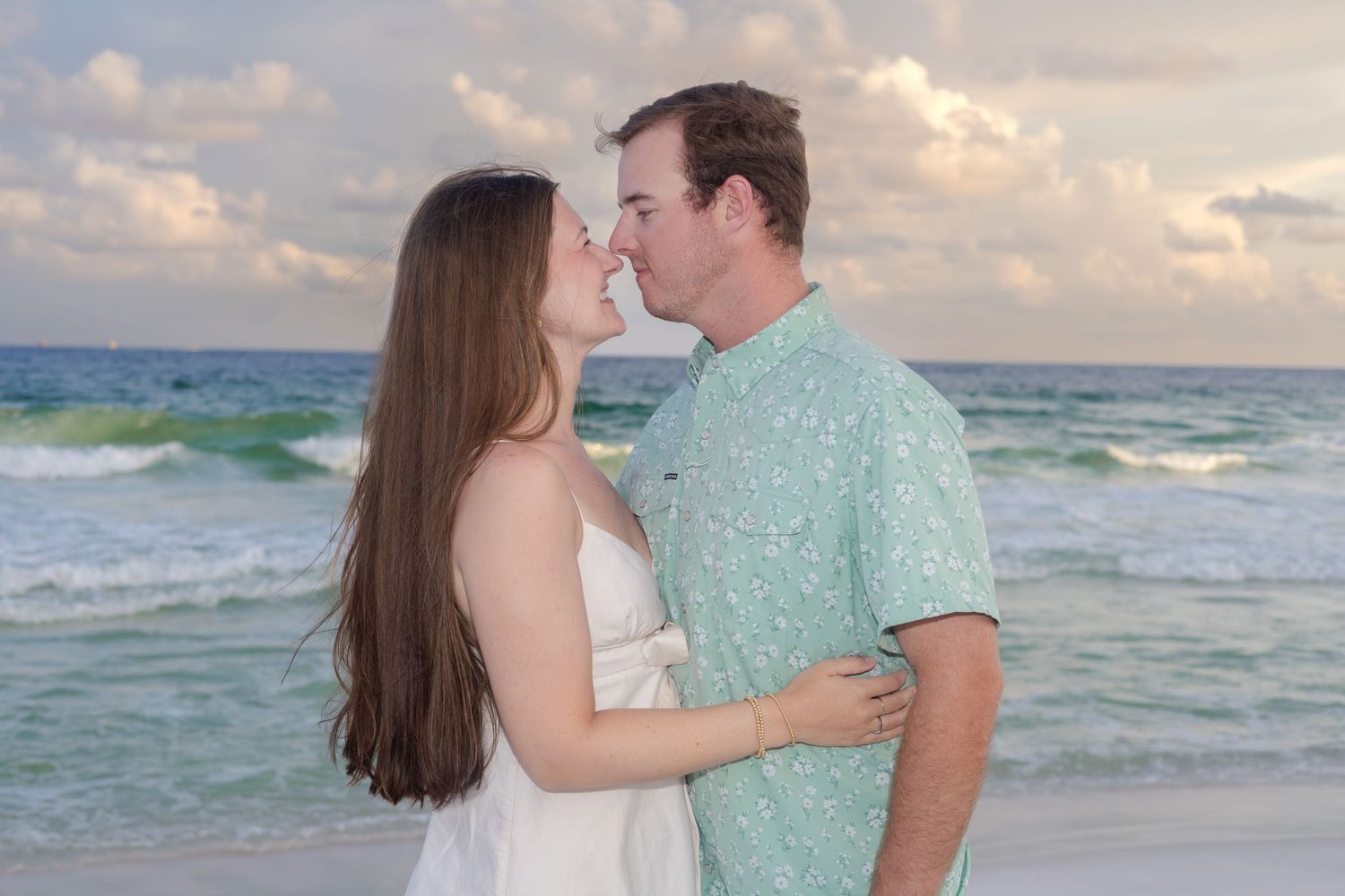 Couple sharing an intimate moment on the beach with gentle waves and warm sunset lighting.