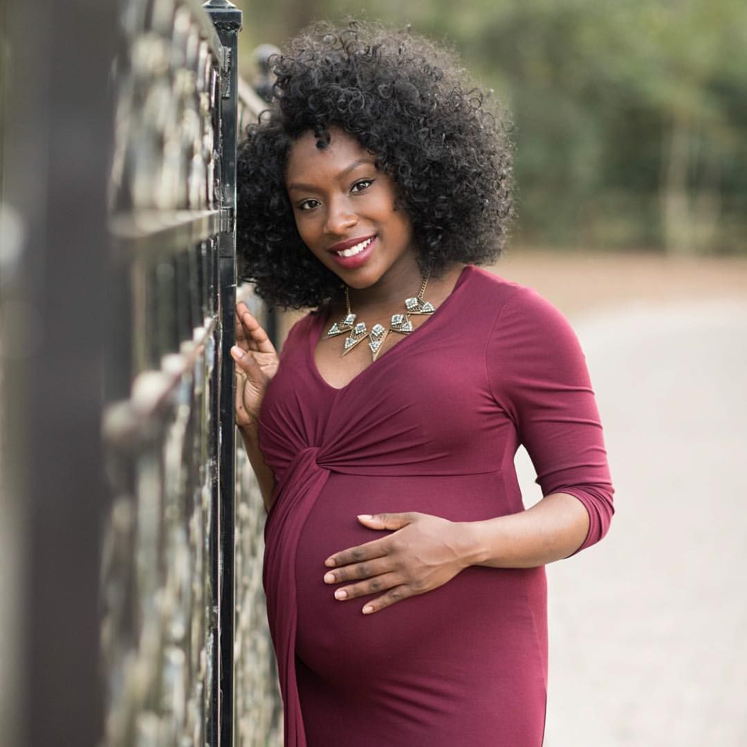 Smiling person in burgundy dress poses outdoors against blurred natural background.