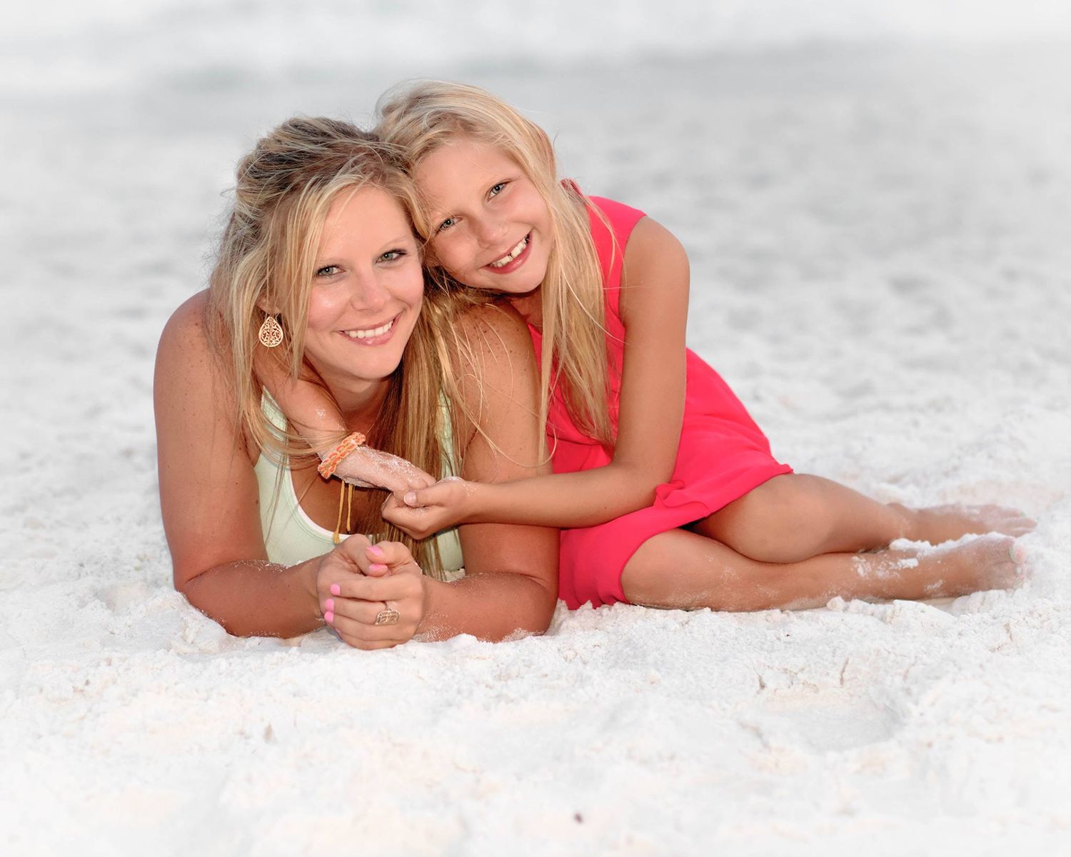 Two people in casual summer attire lying together on white sand at the beach.