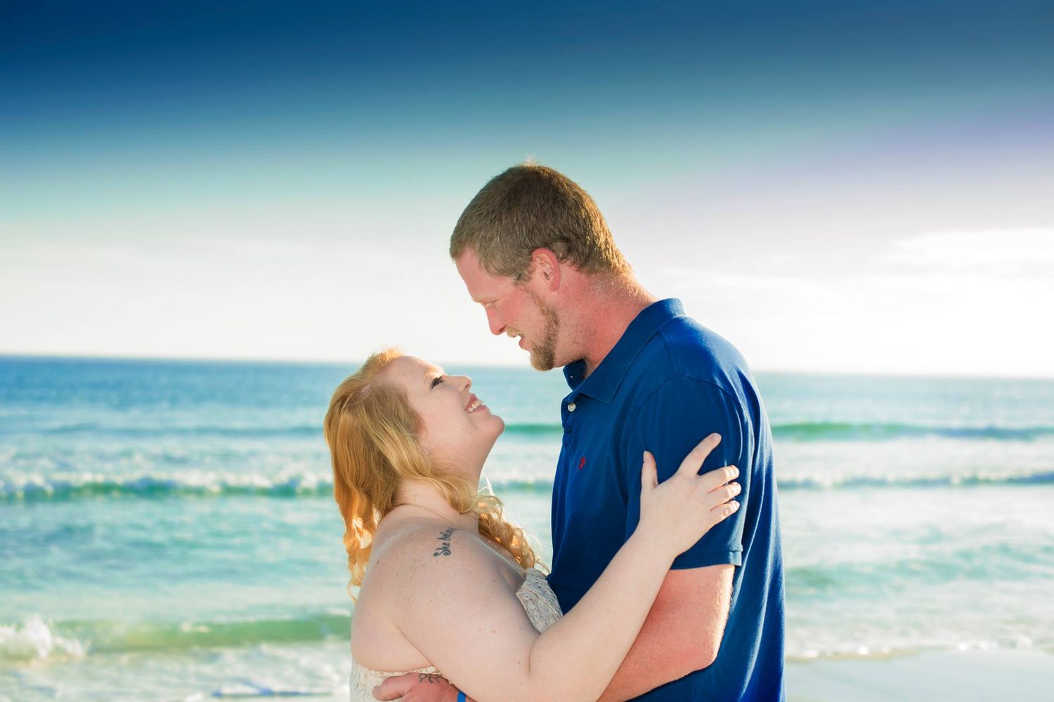 A romantic couple shares tender moments on a beach with turquoise ocean waves and blue sky in the background.