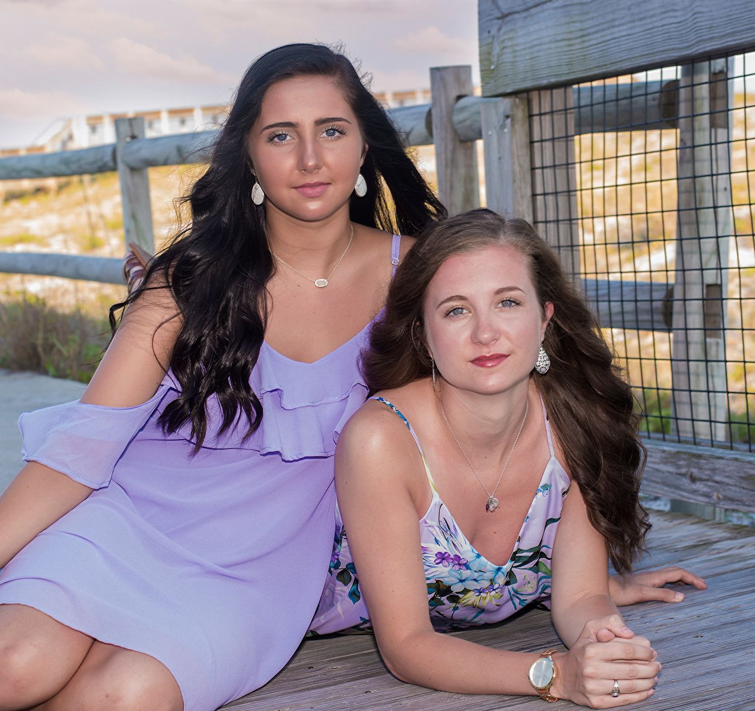 Two friends in summer dresses pose together on a wooden deck during golden hour.