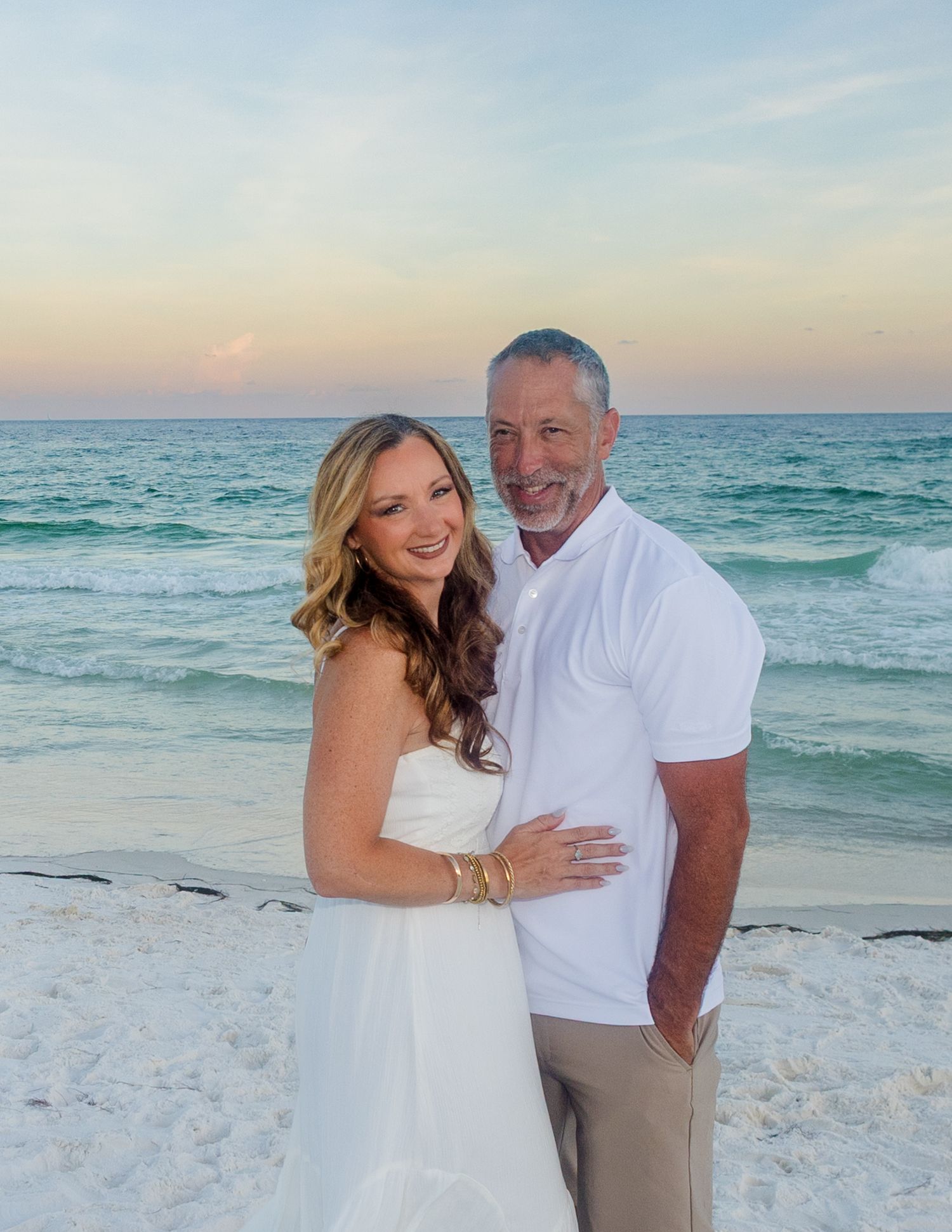 Couple embracing on pristine white sand beach with turquoise ocean waters in background.