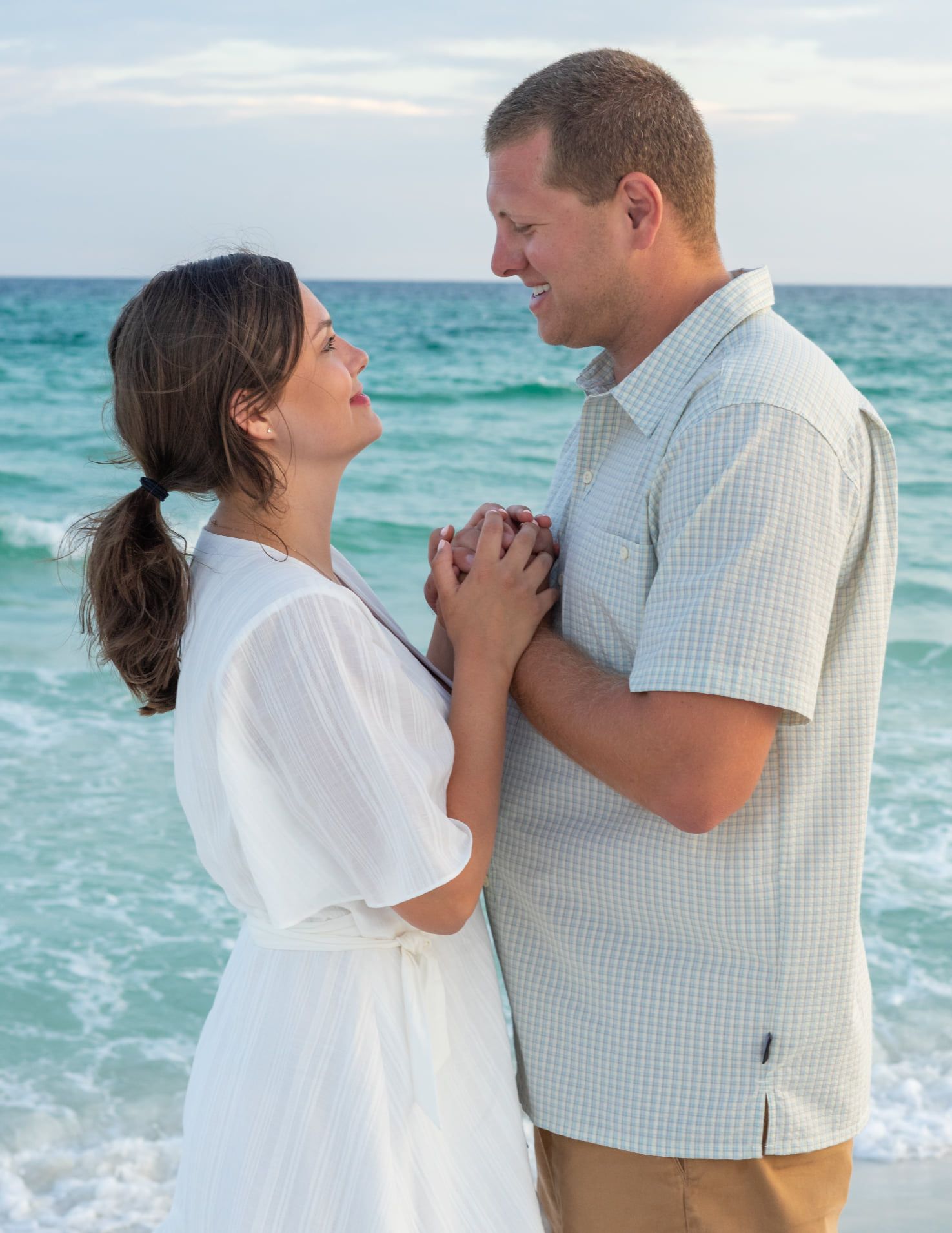 Romantic couple embracing on a beach at sunset with waves crashing behind them.