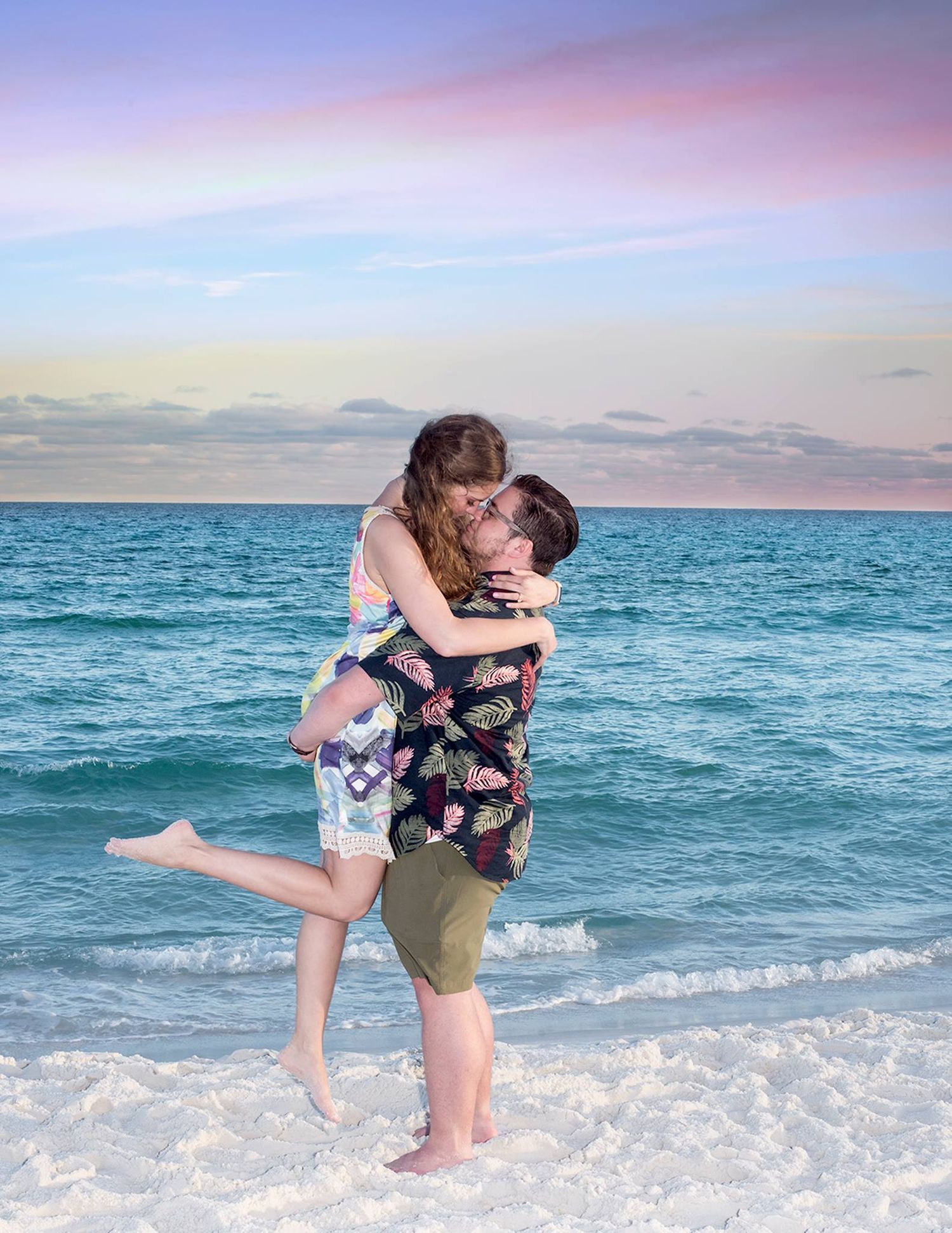 A couple shares a romantic moment at sunset on a beach with turquoise waves crashing behind them.