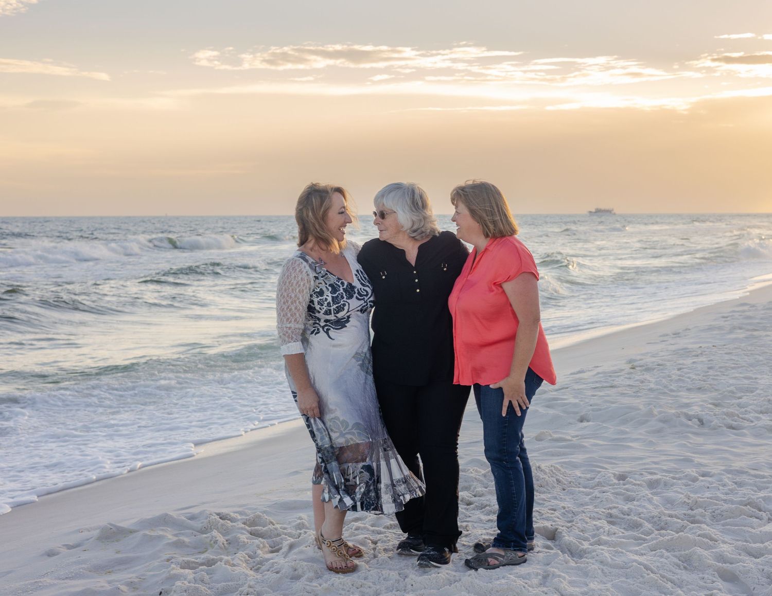 A group of people walk along a sandy beach at sunset with waves crashing on the shore in the background.