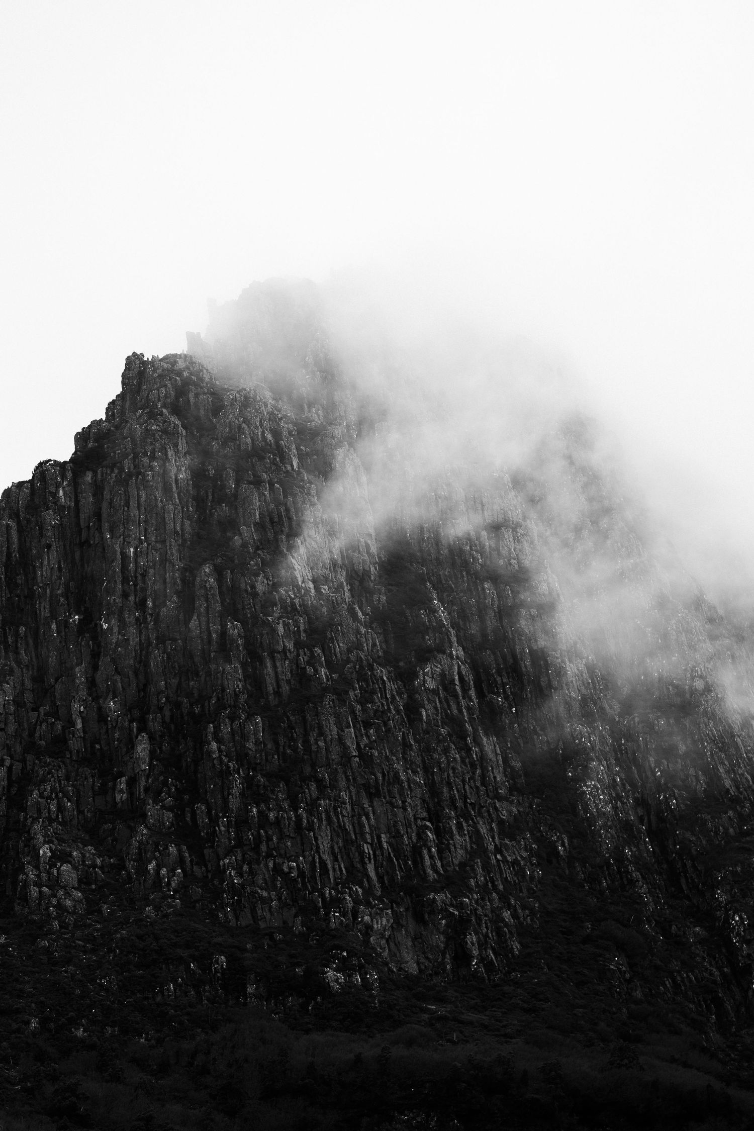 Dramatic black and white mountain peak shrouded in misty clouds against a white sky.