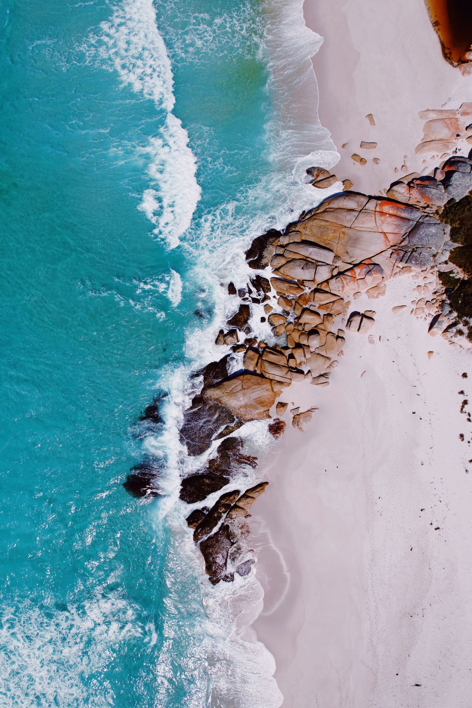 Aerial view of turquoise ocean waves crashing against rocky coastline with white sandy beach.