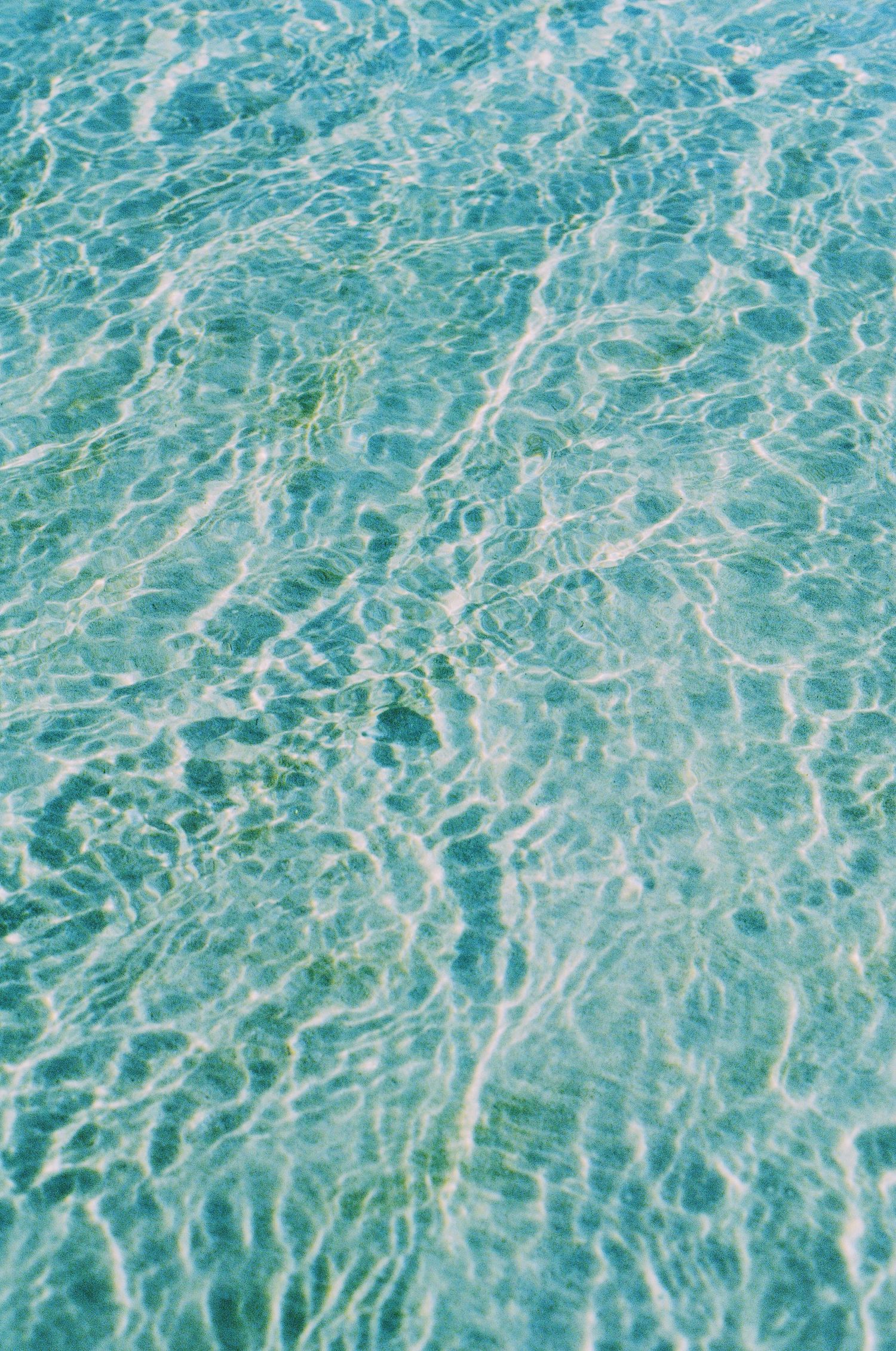 Crystal clear turquoise water creates intricate ripple patterns on a sunny day.