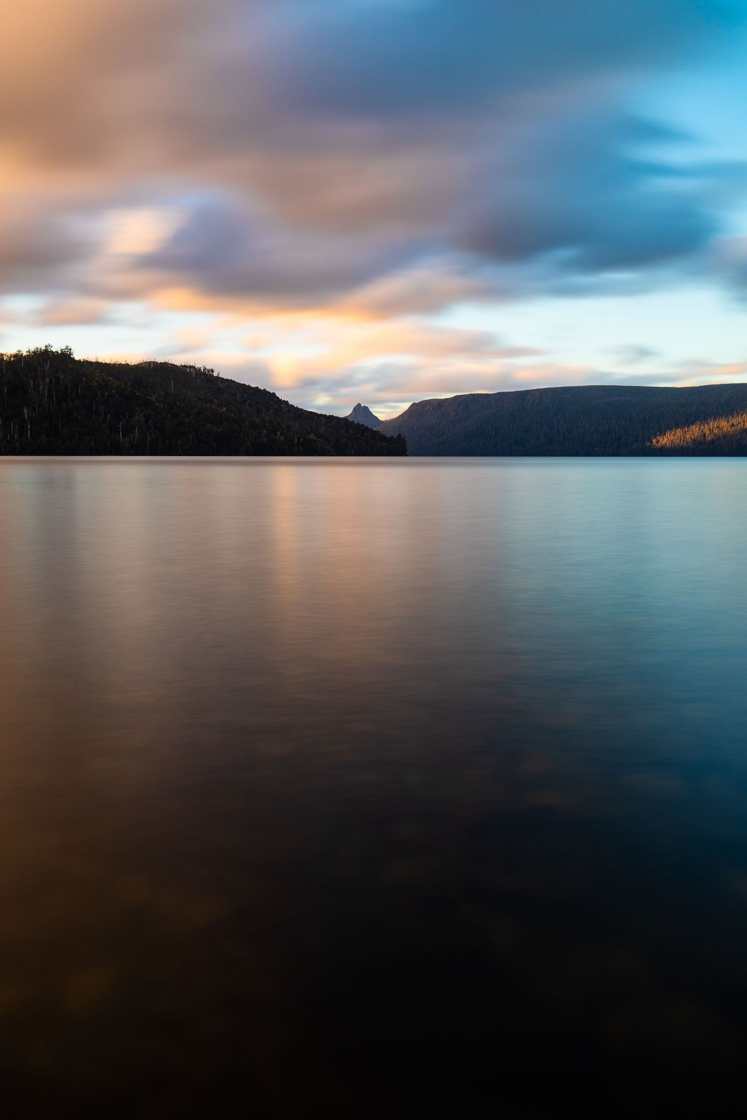 Serene lake at sunset with mountains silhouetted against colorful clouds reflecting on calm waters.