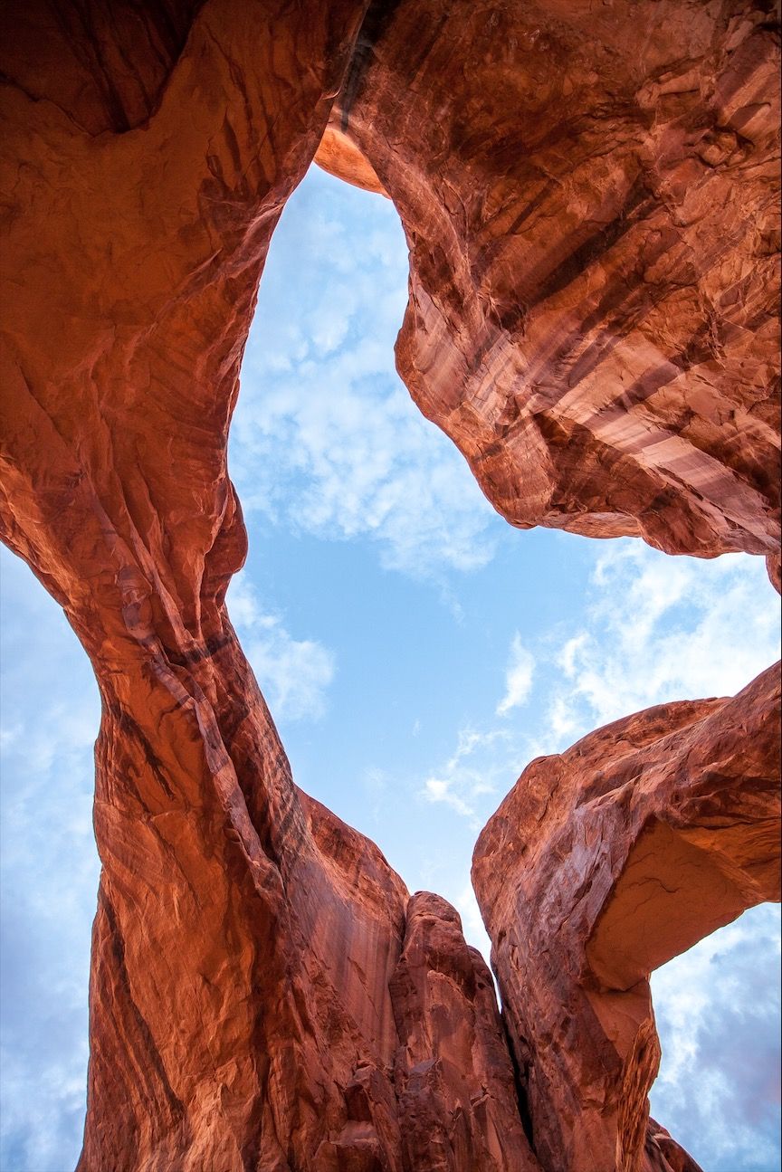 Looking up at dramatic red rock formations and natural arches against a blue sky in Arches National Park, Utah.