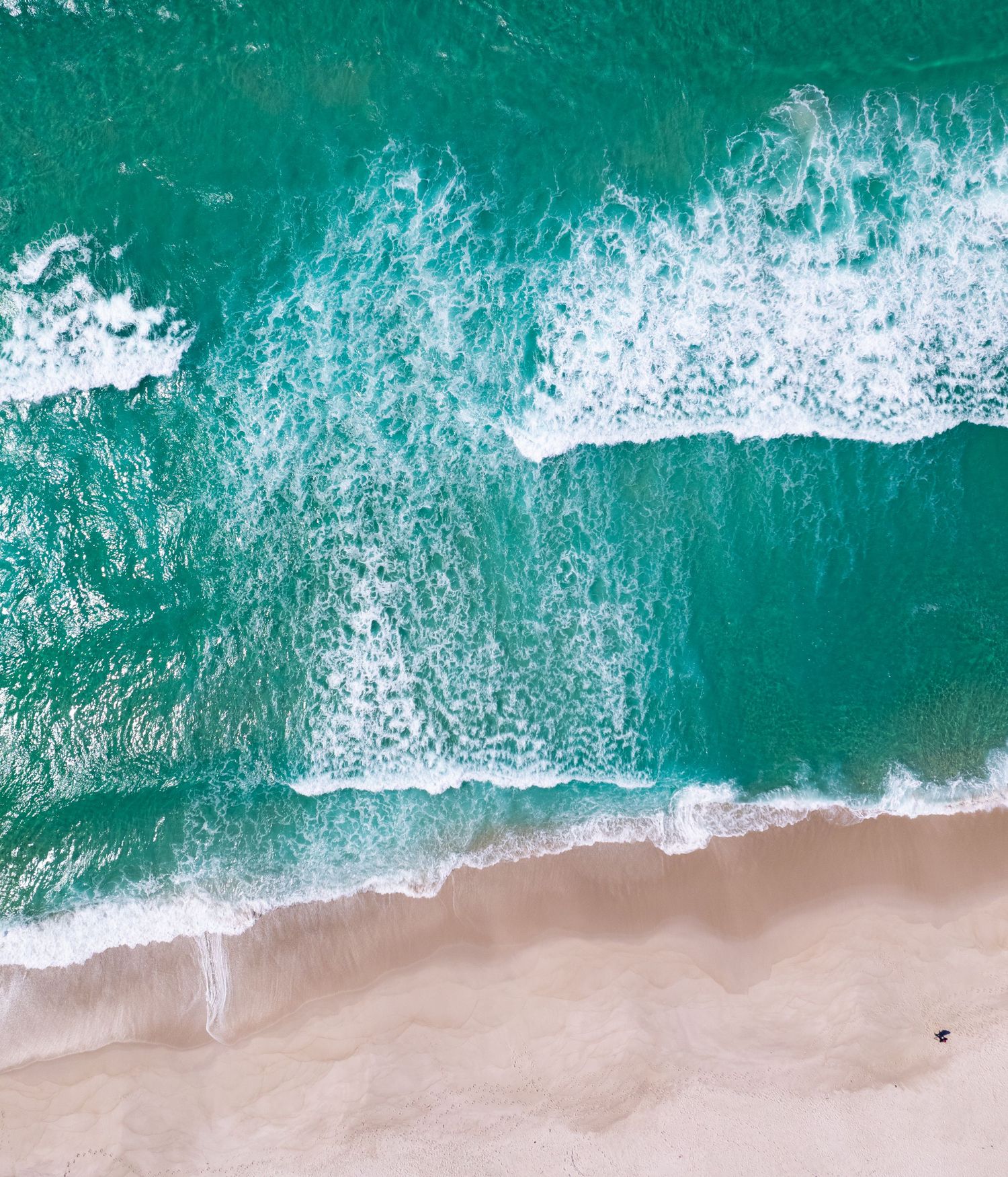 Aerial view of turquoise ocean waves crashing onto sandy beach shore.