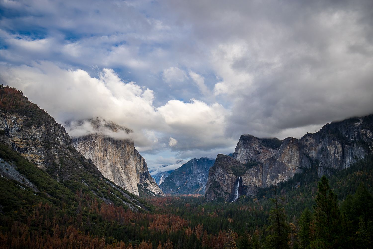 Dramatic view of Yosemite Valley with El Capitan and Half Dome under stormy clouds at sunset.