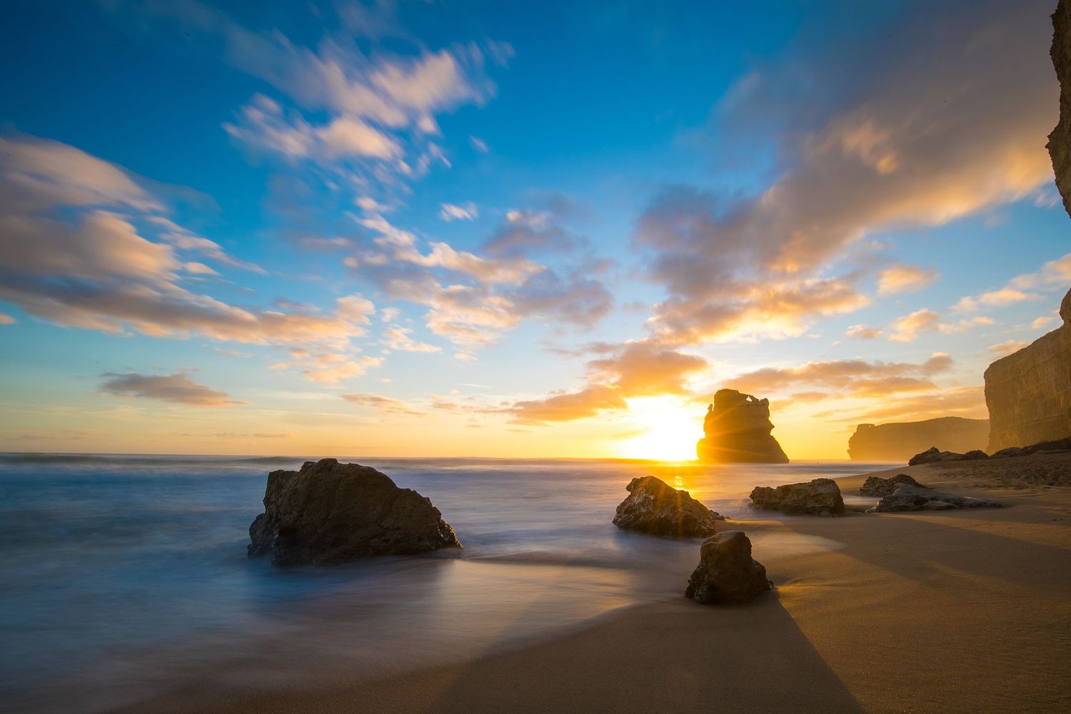 Coastal seascape at sunset with rock formations and cliffs along peaceful beach.
