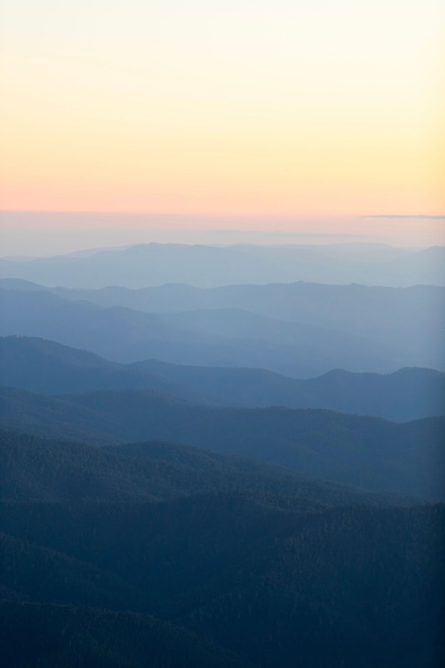 Layered mountain ranges create misty blue ridges against a pastel sunset sky.