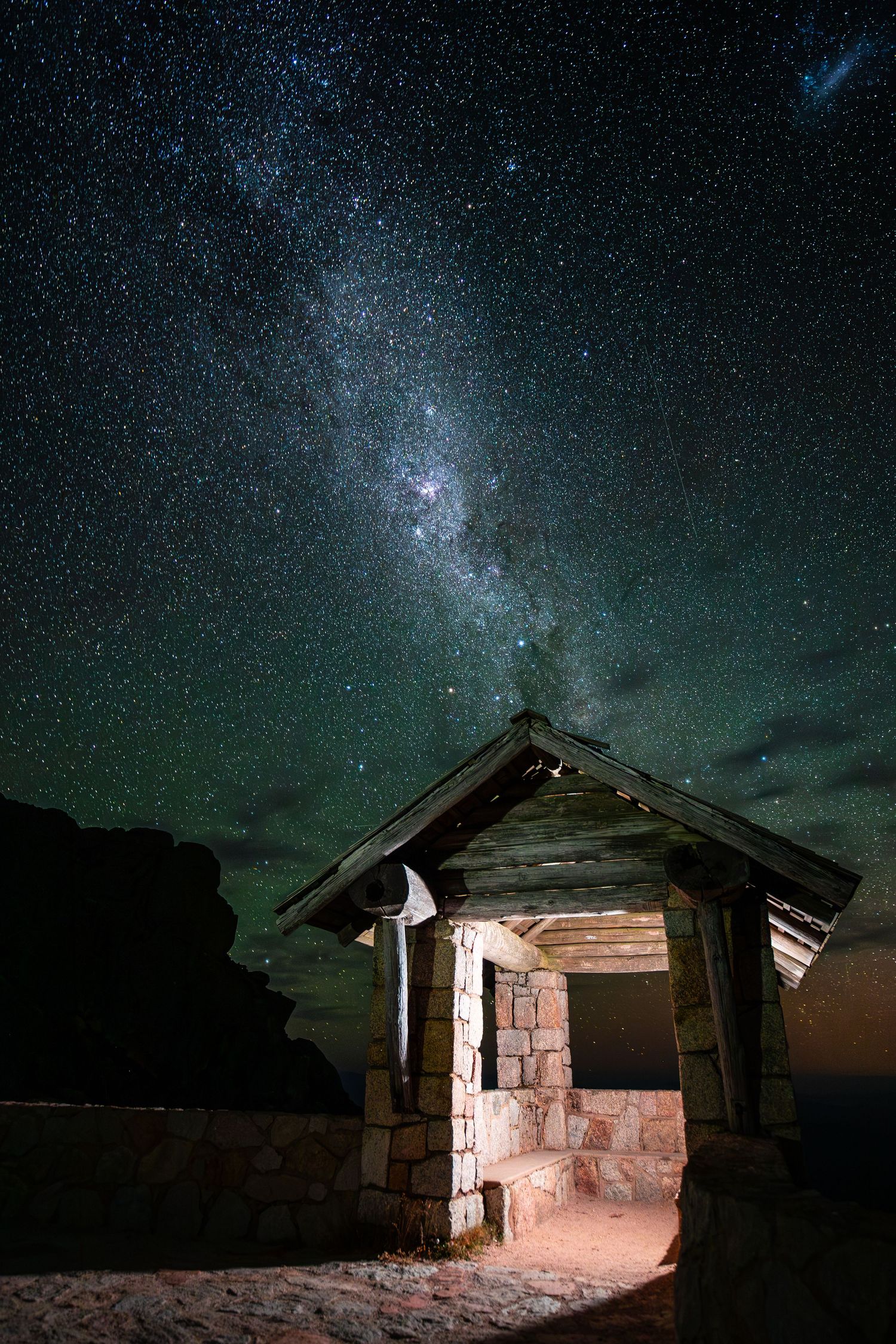 A stone hut illuminated from within glows beneath the Milky Way galaxy and starry night sky.