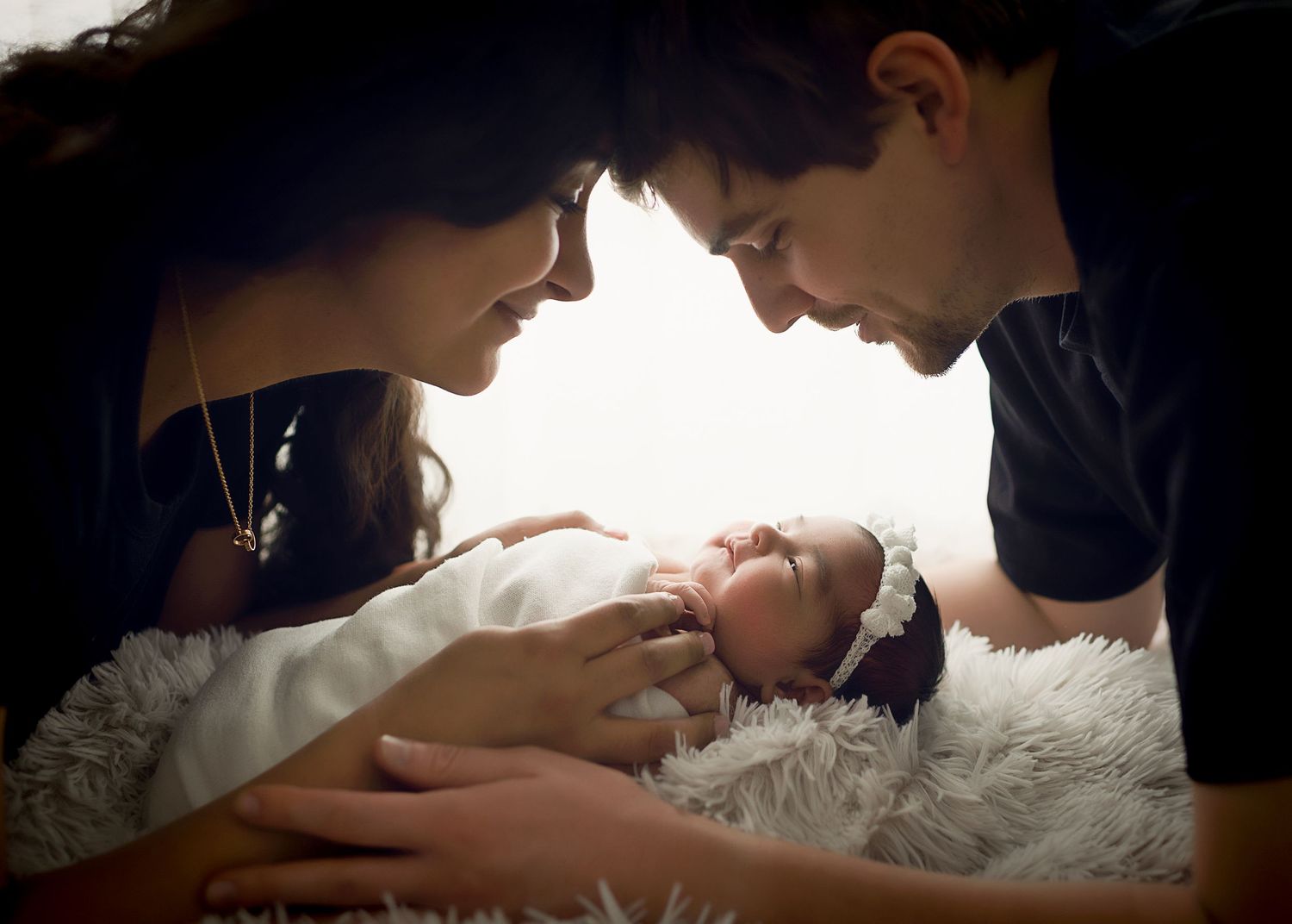 Dramatic lighting captures tender family moments with newborn on textured white surface.
