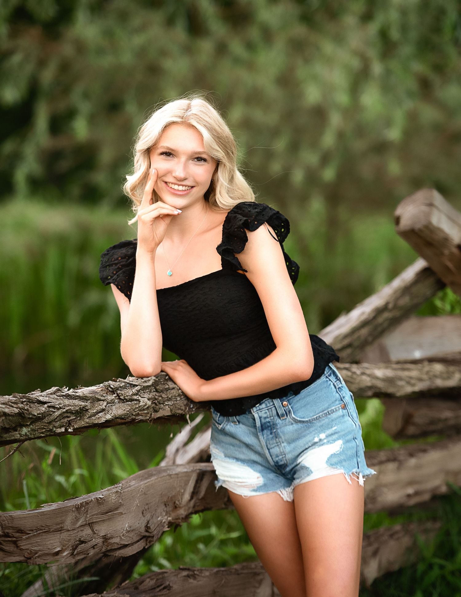 Summer portrait session with denim shorts and black top against natural outdoor setting.